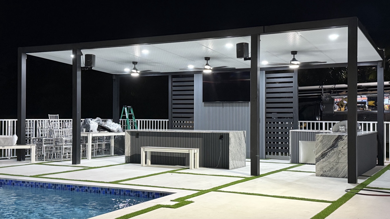 Illuminated aluminum pergola and kitchen next to a swimming pool