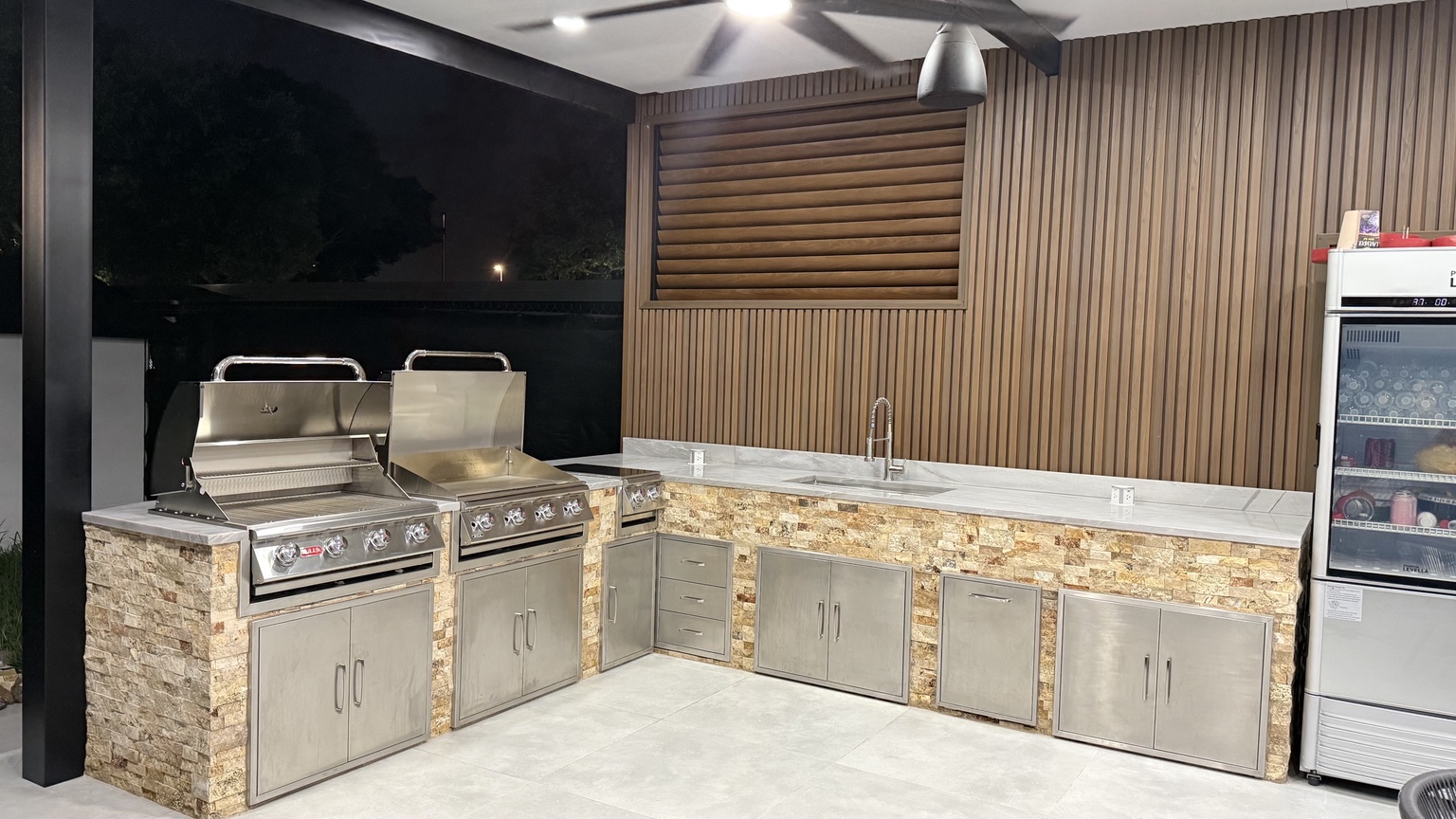 Custom outdoor kitchen finished with natural stone and wood-look aluminum wall panels